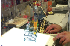 A person using a SALS control box with a test tube with an orange liquid.