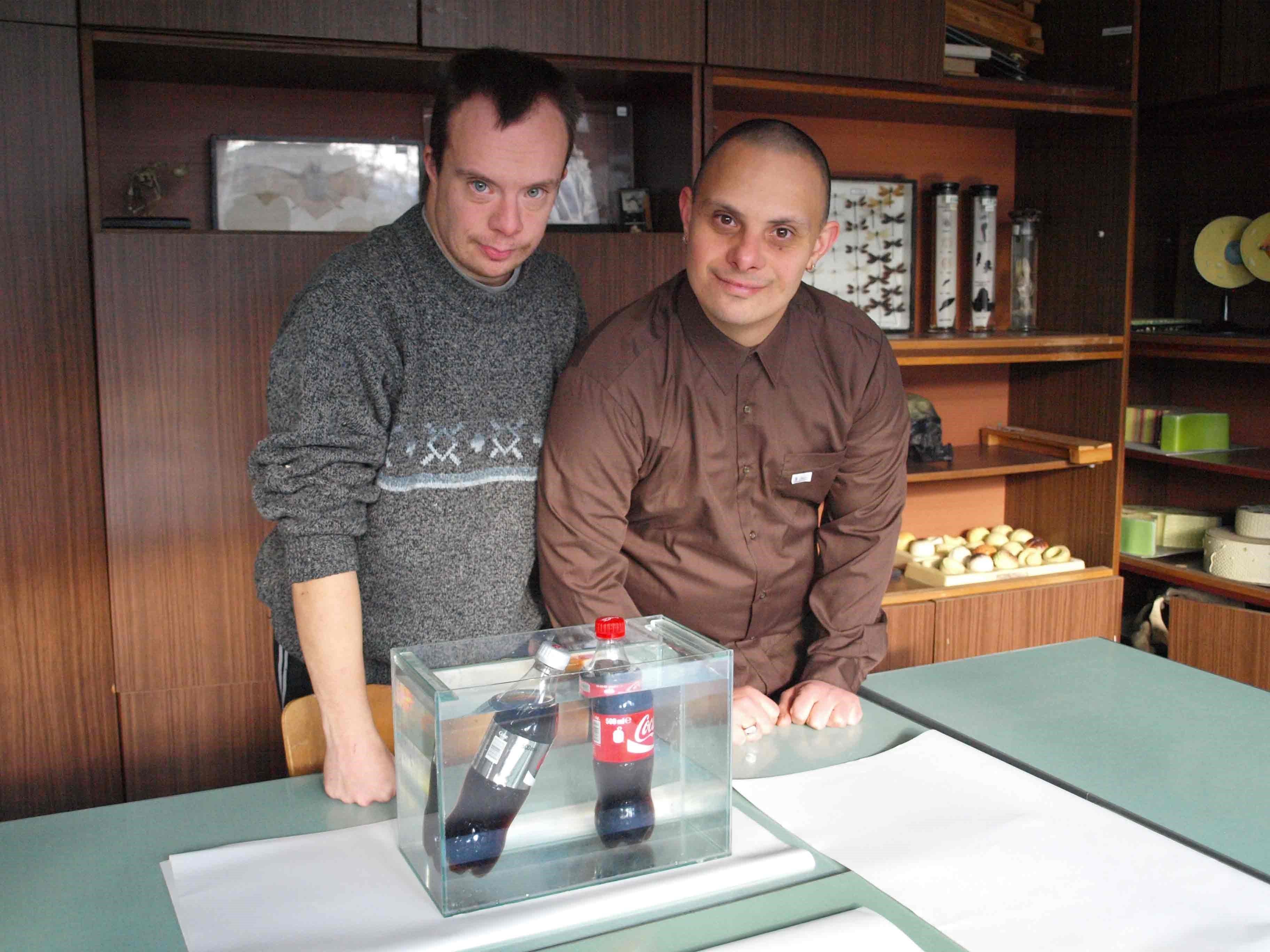 Students next to a tank of water with two bottles, one of Coca-Cola and one of Coca-Cola Light submerged.