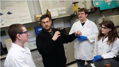 A person teaching with 3 people in lab coats surrounding.