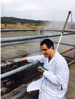 A person next to a railing wearing a lab coat, holding a white cane and a LabQuest Vernier device.