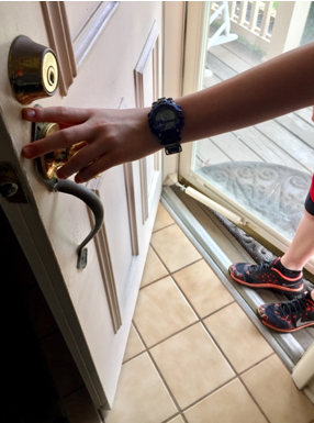 A photograph of a person holding open a door from the outside of a house.