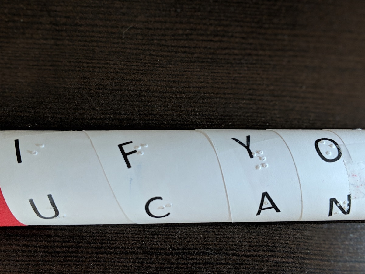 The strip of paper wrapped around a rod, with the letters spelling out 'if you can', with braille below each letter.