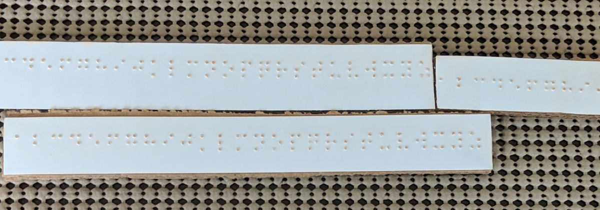 Three strips of paper with braille on each.