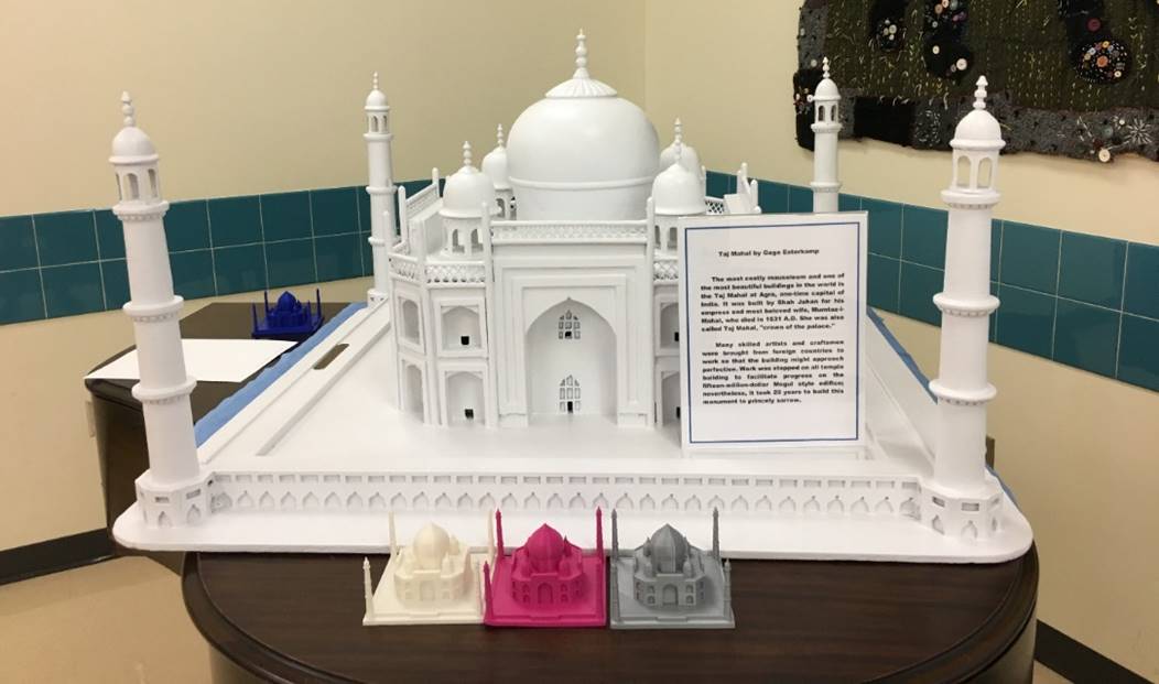 A white 3D printed model of Taj Mahal on a table. In front are 3 smaller versions in different colors (cream, magenta, gray).